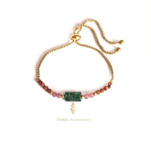 May include: Gold-coloured adjustable bracelet with a rectangular green gemstone, pink and gold beads. The bracelet has a delicate chain and a sliding clasp. The text "Ethnic Accessories" is printed below the bracelet.