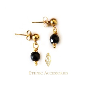 May include: A pair of gold earrings with black gemstone drops. The earrings have a simple stud design with a small gold ball at the top and a dangling black gemstone.