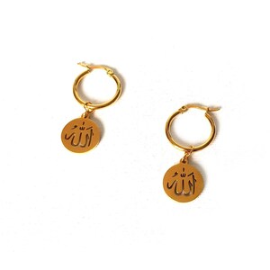 May include: Gold hoop earrings with a dangling charm featuring the Arabic word "Allah" in a cut-out design.