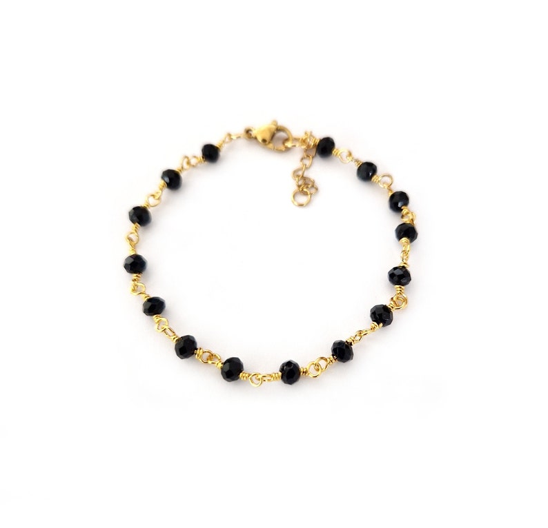May include: A delicate bracelet featuring small, faceted black beads strung on gold-colored wire. The bracelet has a gold-colored clasp and is displayed against a white background. The jewelry is suitable for everyday wear or special occasions.