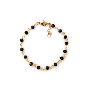 May include: A gold-colored bracelet featuring a series of small, faceted black beads strung together. The beads are connected by a delicate gold wire, and the bracelet has a clasp closure. The bracelet is displayed on a white background.