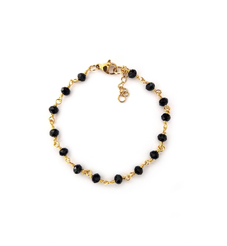 May include: A gold-colored bracelet featuring a series of small, faceted black beads strung together. The beads are connected by a delicate gold wire, and the bracelet has a clasp closure. The bracelet is displayed on a white background.