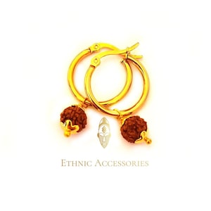 May include: Gold hoop earrings with brown bead charms. The beads are made of rudraksha, a sacred seed used in Hinduism.