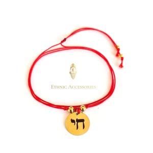 Può includere: Braccialetto con cordino rosso con un ciondolo circolare color oro con una lettera ebraica. Il braccialetto ha perline color oro e il testo "Ethnic Accessories".
