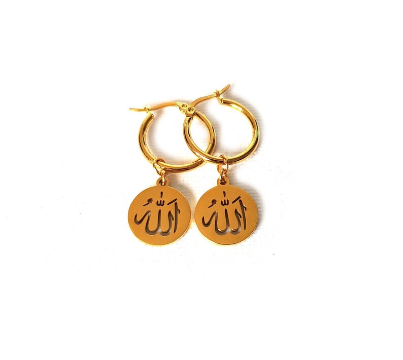May include: Gold hoop earrings with a dangling charm featuring the Arabic word "Allah" in a cut-out design.