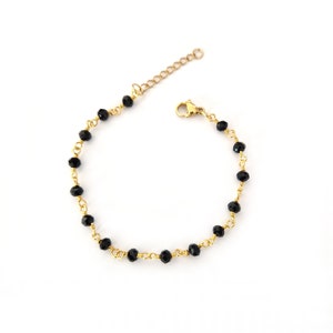 May include: A delicate gold-toned bracelet featuring small, faceted black beads strung along a fine chain. The bracelet has an adjustable length and a secure clasp, suitable for everyday wear.