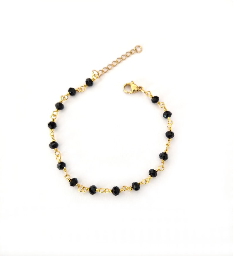 May include: A delicate gold-toned bracelet featuring small, faceted black beads strung along a fine chain. The bracelet has an adjustable length and a secure clasp, suitable for everyday wear.