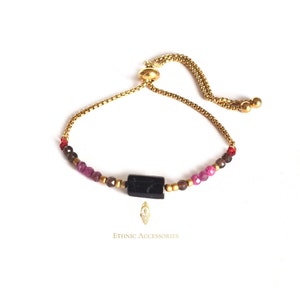 May include: A gold chain bracelet with a black stone charm and red, pink, and brown beads. The bracelet has a sliding clasp.