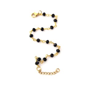 May include: A delicate bracelet featuring black faceted beads strung on a gold-colored chain. The bracelet has a lobster clasp closure and an adjustable chain for a customizable fit. The beads are evenly spaced along the chain.