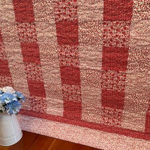May include: A red and white patchwork quilt with a floral pattern. The quilt features a checkerboard design with alternating blocks of solid red and white floral fabric. The quilt is made of soft fabric and is suitable for a bed or as a decorative throw.