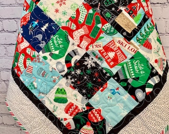 May include: A patchwork quilt with a winter theme. The quilt is made of various fabrics with different patterns, including snowflakes, mittens, and Christmas trees. The quilt is edged with a black and white polka dot fabric.