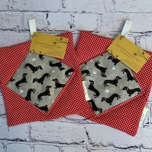 May include: Two square pot holders with a red and white polka dot pattern. The center features a gray square with black dachshund dogs and white snowflakes. Each pot holder has a tag that reads "Autumn Country Crafts."
