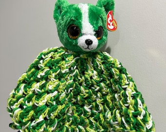 May include: A green and white plush bear with large, brown eyes and a red tag. The bear is attached to a green, white, and yellow crocheted blanket. The blanket is made of a soft, textured yarn.