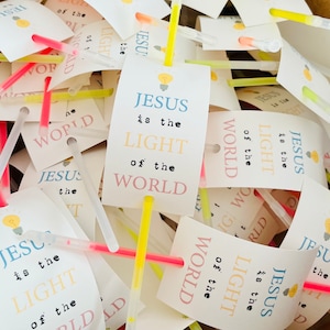 May include: A pile of glow sticks with tags that say "Jesus is the light of the world". The tags are in various colours, including pink, blue, and yellow.