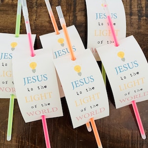 May include: Five glow sticks with white paper tags attached. The tags have a lightbulb graphic and the text "JESUS is the LIGHT of the WORLD".