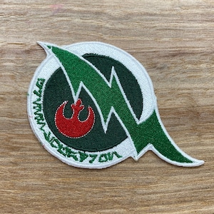 Könnte beinhalten: Ein weißer, grüner und roter gestickter Aufnäher mit einem grünen Blitzdesign und dem Text "Wedge Antilles X-Wing Squadron" am Rand.