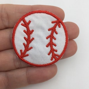 May include: A white baseball patch with red stitching. The patch is about 2 inches in diameter.