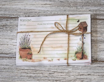 May include: A stack of recipe cards with a watercolor design of a birdhouse, lavender, and potted plants. The cards are tied together with twine and have the words "Recipe:" and "From the kitchen" printed on them.