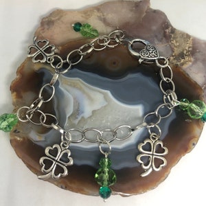 May include: A silver chain bracelet with four silver four-leaf clover charms and green glass beads.