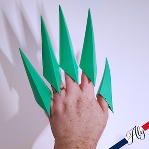 May include: A set of six green finger claws, made of plastic, worn on a hand. The claws are pointed and sharp, and they are designed to look like the claws of a predator.