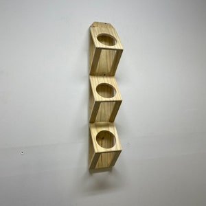 May include: A wooden wall-mounted shelf with four circular openings. The shelf is made of light-colored wood and has a simple design.