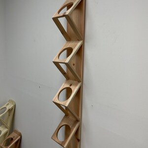 May include: A wooden wall-mounted storage rack with five slots for holding items like mugs or glasses. The rack is made of natural wood and has a simple, rustic design.