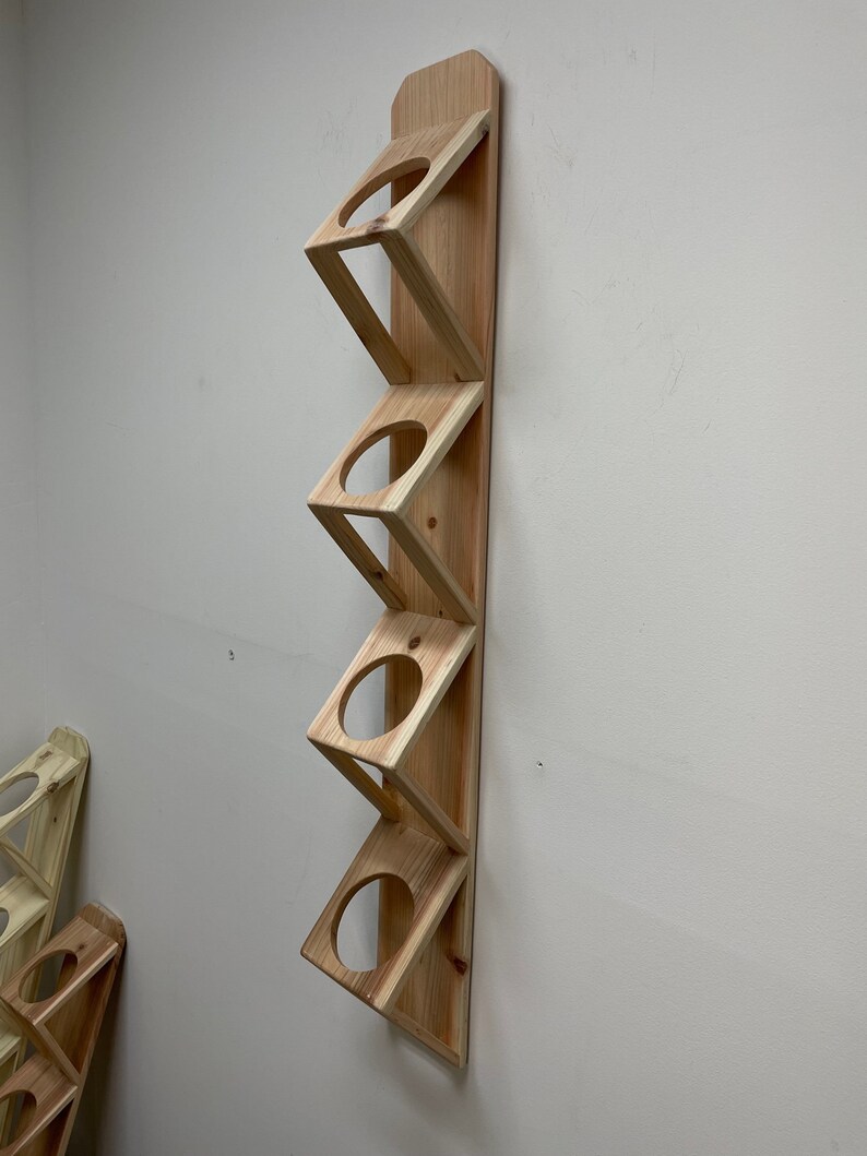 May include: A wooden wall-mounted storage rack with five slots for holding items like mugs or glasses. The rack is made of natural wood and has a simple, rustic design.