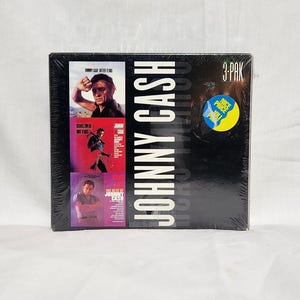 Può includere: Un set di 3 CD con Johnny Cash. La copertina anteriore presenta una foto in bianco e nero di Johnny Cash con il testo "Johnny Cash" in lettere bianche. La copertina posteriore presenta una foto a colori di Johnny Cash con il testo "The Best of Johnny Cash" in lettere bianche. Il set di CD è confezionato in una custodia di plastica trasparente.