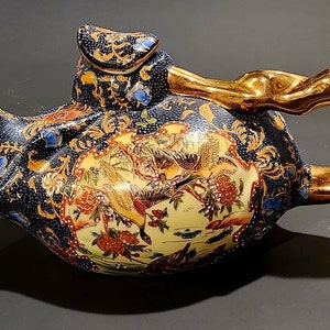 Könnte beinhalten: Eine blaue und goldene Teekanne mit floralem Muster und goldenem Henkel. Die Teekanne hat eine einzigartige Form und ist mit aufwendigen Details verziert.