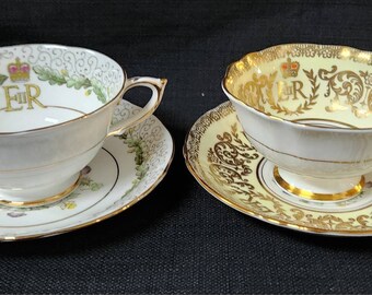 Könnte beinhalten: Zwei antike Teetassen und Untertassen mit goldenen Verzierungen und Blumendesigns. Die Tassen zeigen das königliche Signet "ER" mit einer Krone darüber.