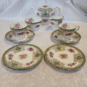 May include: A vintage tea set with a floral pattern. The set includes a teapot, creamer, sugar bowl, two teacups, and two saucers. The teacups and saucers have a green and gold trim.