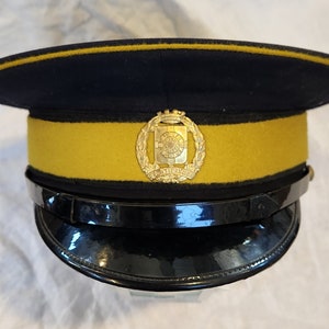 Puede incluir: Un sombrero de estilo militar negro y dorado con una insignia dorada que presenta una corona y las palabras "City of Liverpool".