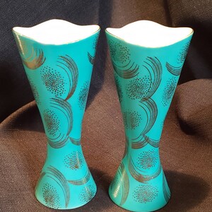 May include: A pair of teal blue ceramic candle holders with a gold and black geometric pattern. The holders have a flared top and a narrow base.