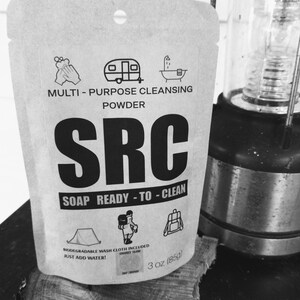 Könnte beinhalten: Ein brauner Papierbeutel mit dem Text "SRC SOAP READY-TO-CLEAN" und Illustrationen eines Zeltes, einer Person mit einem Rucksack und einem Rucksack. Der Beutel enthält auch den Text "MULTI-PURPOSE CLEANSING POWDER" und "3 oz (85g)".