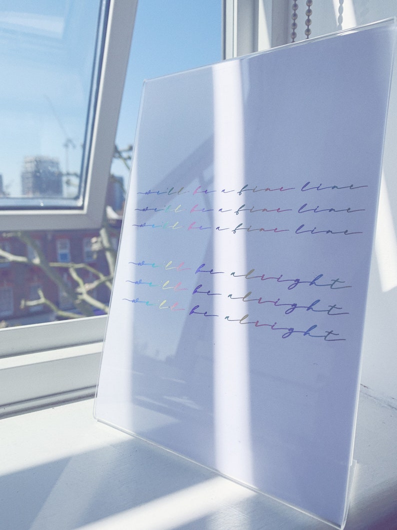 Foiled text on paper that reads "we'll be a fine line" three times and then "we'll be alright" three times in cursive.