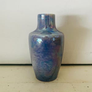 May include: A small, iridescent blue and purple ceramic vase with a rounded body and a narrow neck.