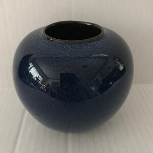 May include: A dark blue ceramic vase with a speckled glaze and a black rim.
