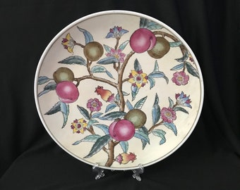May include: A white ceramic plate with a floral design featuring a tree branch with pink and green fruit, yellow and blue flowers, and green leaves.