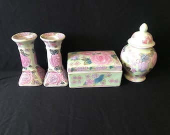 May include: A set of four porcelain items featuring floral designs in shades of pink, green, and gold. The set includes two candle holders, a small box, and a lidded jar.