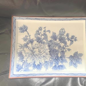 May include: Rectangular ceramic tray with a floral design in shades of blue and white. The tray features a large peony and other flowers and leaves. The border is a combination of blue and red. A decorative piece for serving or display.
