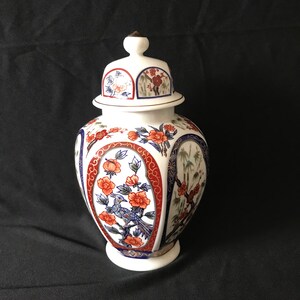May include: White porcelain vase with a lid, decorated with red, blue, and gold floral and bird designs. The vase has a round body and a narrow neck.