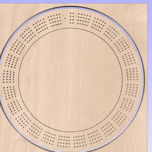 Könnte beinhalten: Ein kreisförmiges Cribbage-Brett aus Holz. Das Brett ist hellbraun und hat eine Reihe kleiner Löcher zum Zählen, die kreisförmig angeordnet sind. Ein hellblauer Rand umgibt das Brett.