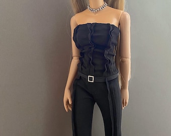 May include: A fashion doll wearing a black strapless jumpsuit with a ruffled bodice and a matching belt with a silver buckle. The doll has long blonde hair, hoop earrings, and a sparkling choker necklace. The doll's outfit is a stylish ensemble.