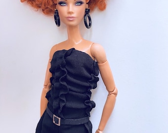 May include: A fashion doll with vibrant red curly hair and dark eye makeup. The doll wears a black strapless top with ruffled detailing, black pants, and large black hoop earrings. A thin black belt with a silver buckle cinches the waist.