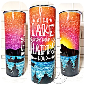 May include: A stainless steel tumbler with a colorful glitter design and a white silhouette of a lake scene with a boat and trees. The text "At the Lake Every Hour is Happy Hour" is printed on the tumbler.