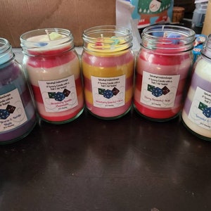 May include: A collection of glass jar candles with layered wax in various colors. Each candle has a label with text and a small dice graphic. The candle scents include Ocean Breeze, Strawberry Vanilla, Cherry Blossom, and Lavender Vanilla. Each candle is 10.5 ounces.