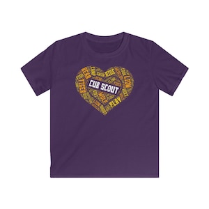 Könnte beinhalten: Ein lila T-Shirt mit einem herzförmigen Design, das mit Wörtern gefüllt ist, die mit Pfadfindern in Verbindung stehen, wie z. B. "schwimmen", "fahren" und "spielen". Die Wörter sind in Gelb und Weiß gehalten und bilden einen Kontrast zum Hintergrund.