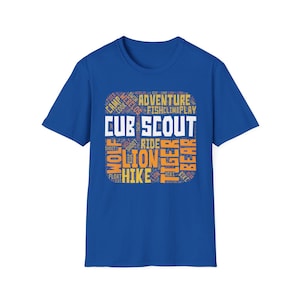 Könnte beinhalten: Ein königsblaues T-Shirt mit einem rechteckigen Design. Das Design enthält die Worte "CUB SCOUT" in Weiß, umgeben von Wörtern wie "ADVENTURE", "HIKE" und "BEAR" in Orange und Weiß. Das T-Shirt besteht aus einem weichen Material.