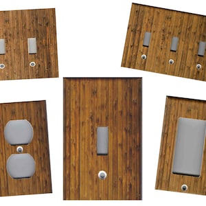 May include: A collection of wooden-look light switch and outlet covers. The covers feature a vertical wood grain pattern in shades of brown. The collection includes covers with one, two, and three switches, as well as an outlet cover.