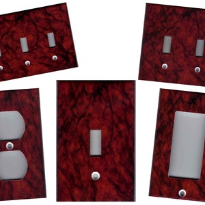 May include: Set of six decorative wall plates featuring a red marble pattern. The plates include a single light switch, a double light switch, a triple light switch, a single outlet, a double outlet, and a single light switch with a dimmer.
